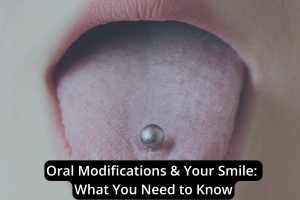 Close-up of an open mouth showcasing a silver tongue piercing. Text overlay reads: "Oral Modifications & Your Smile: Everything You Need to Know.